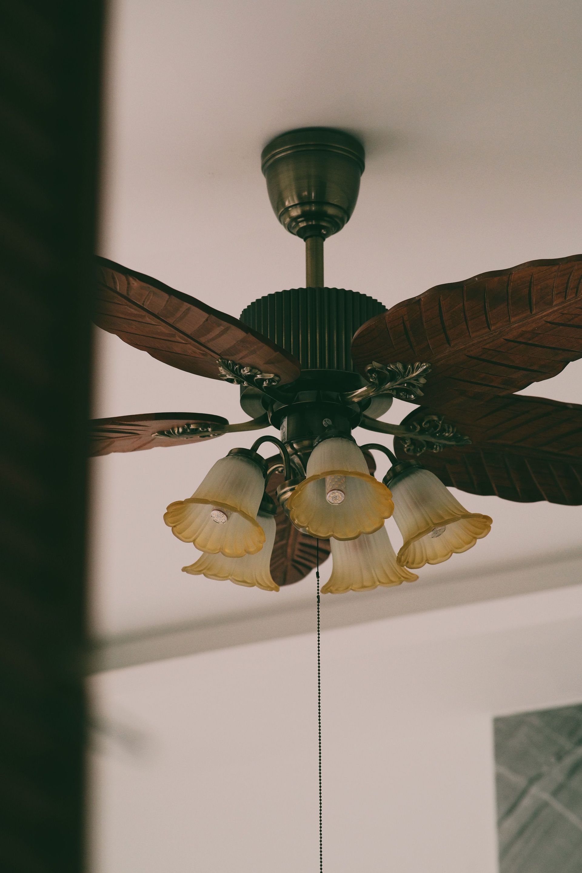 A classic vintage ceiling fan with ornate leaf blade design and floral light fixtures, creating a nostalgic indoor ambiance.